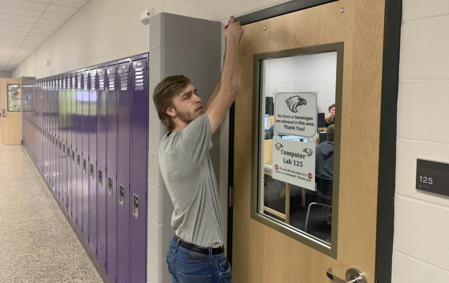 Small engines student Landon Beck takes a small break from working on his engine to lubricate a door hinge for Mrs. Mosher.