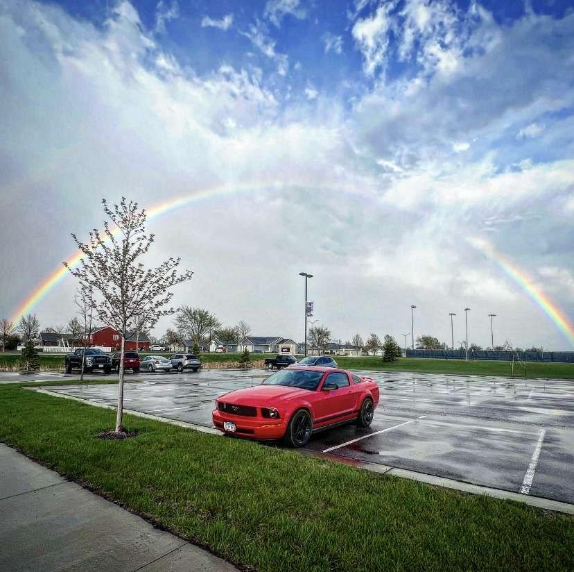 The red stang parked under a rainbow.