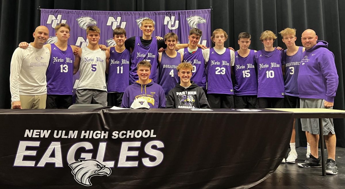 Boys Varsity Basketball team stands behind Colton Benson while he signs his letter of intent.
