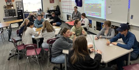 A shot of the Knowledge Bowl team practicing with Mr. Nelson reading.  ... When Mr. Bute asked me if I wanted to help him out I jumped on the opportunity! I really enjoy seeing kids use their brains outside of the classroom and be competitive, stated Mr. Nelson