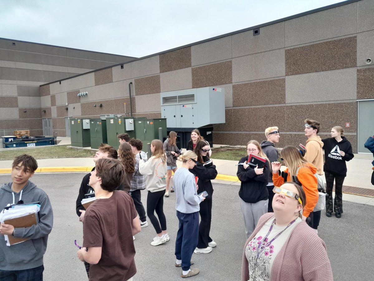 People gather outside the school to catch a glimpse of the eclipse through the clouds