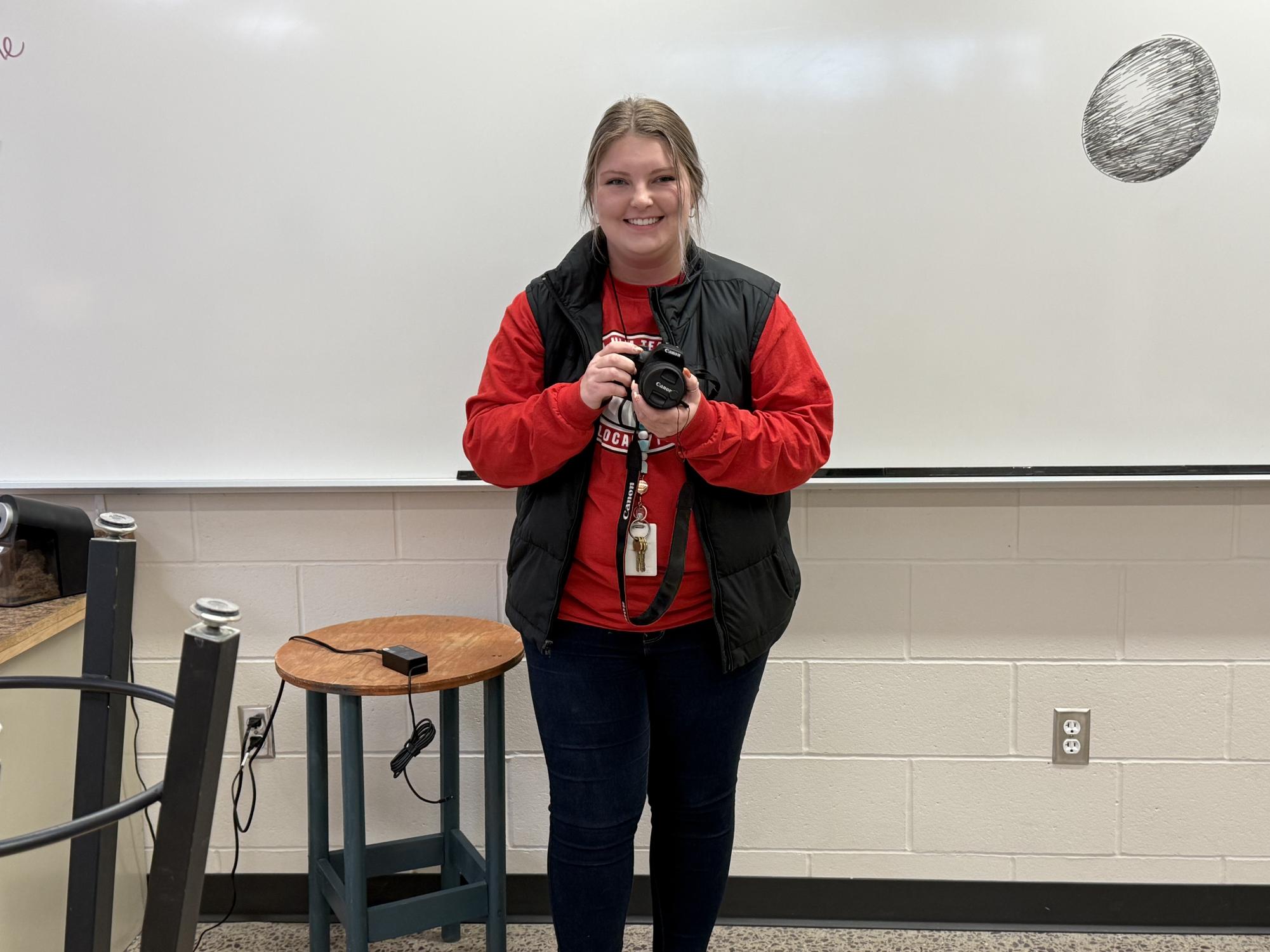 Ms. Page holding a Canon EOS 2000D camera, the standard given to students in the class. 