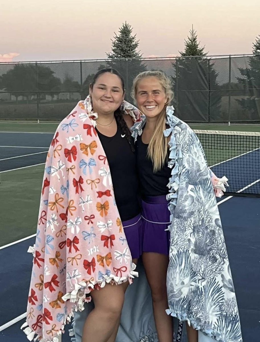 Jocelyn Pettersen and Karlee Prahl in their blankets after their match at the NUHS tennis courts, carrying on the tradition of senior night.