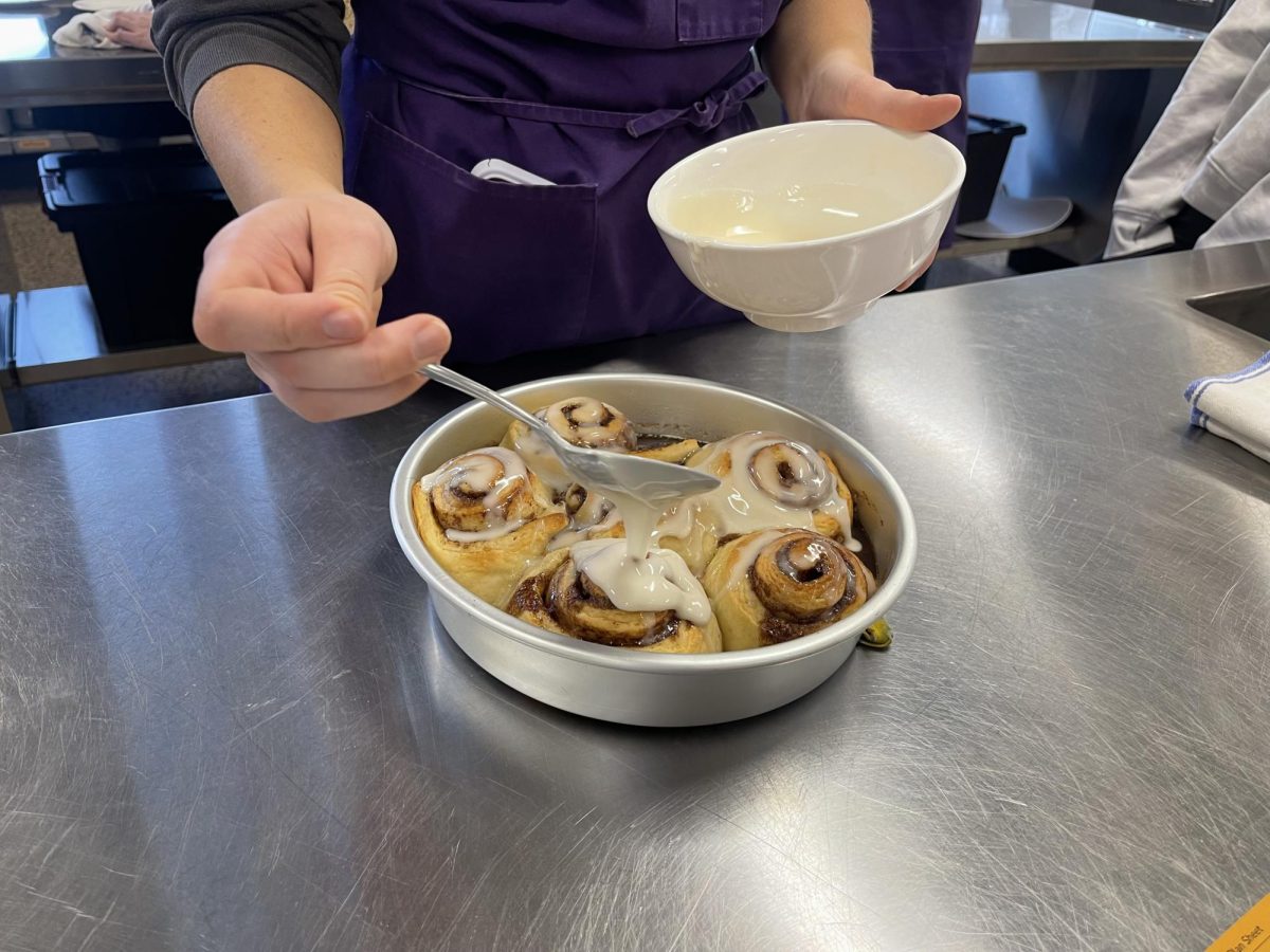 The yummy frosting getting poured on the fresh cinnamon rolls