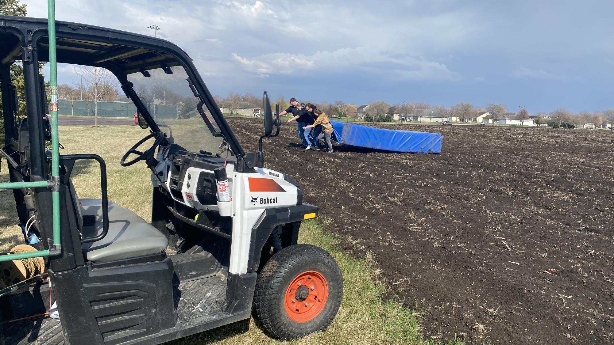 NUHS custodial staff retrieve a track mat that high winds launched into a neighboring farm field Thursday.