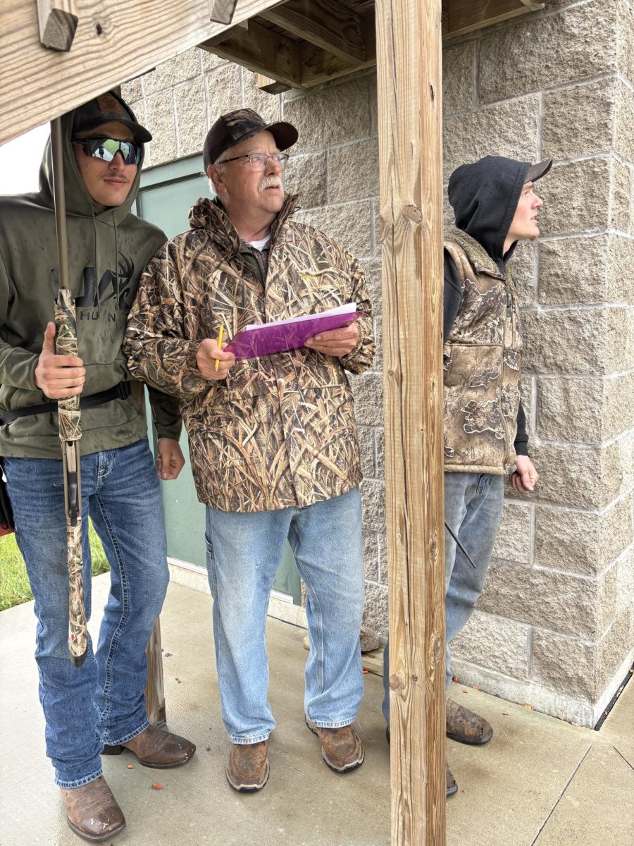 Senior Dylan Armstrong, left staying dry while waiting for his turn to shoot next to head coach James Arndt and volunteer coach Nicholas Syverson. 