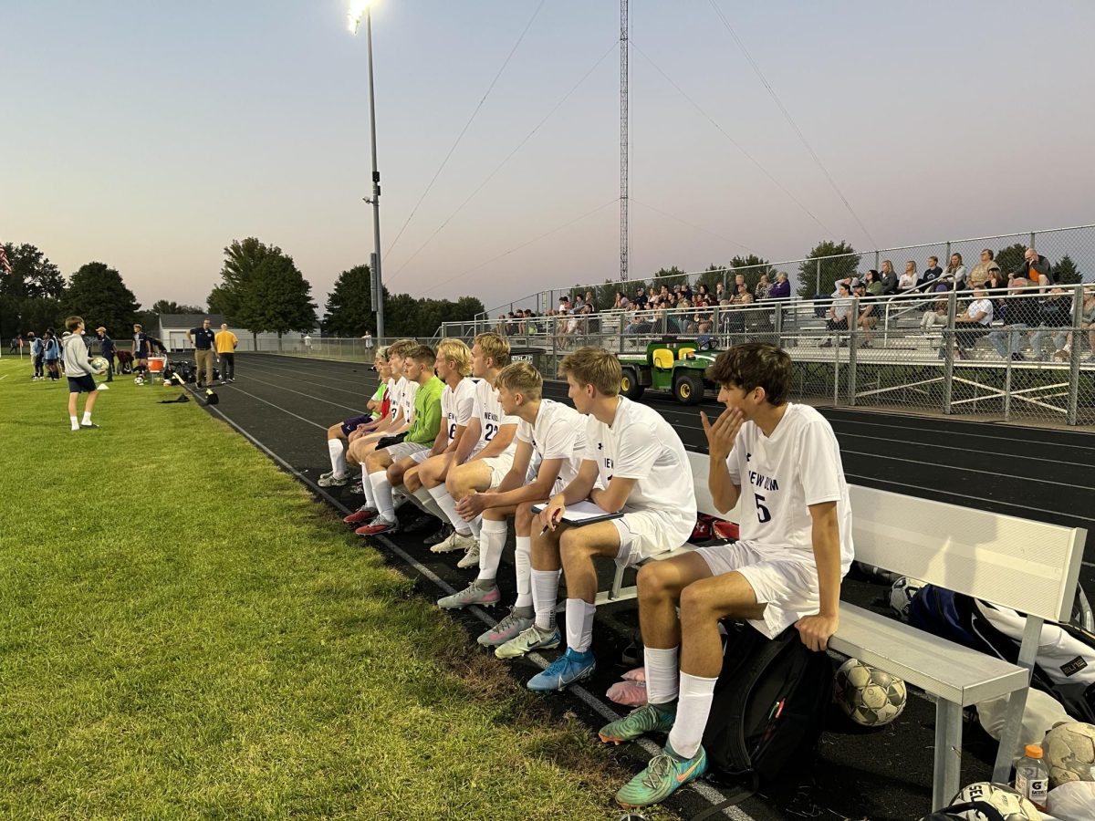 Varsity boys soccer players watch the game while away from home.