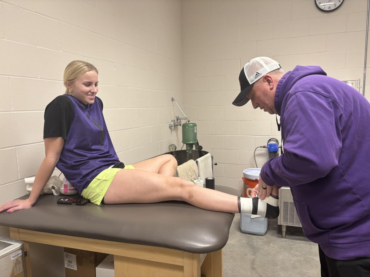 Marcus Hopp (right) is taping Senior basketball player Brooklyn's ankle before practice