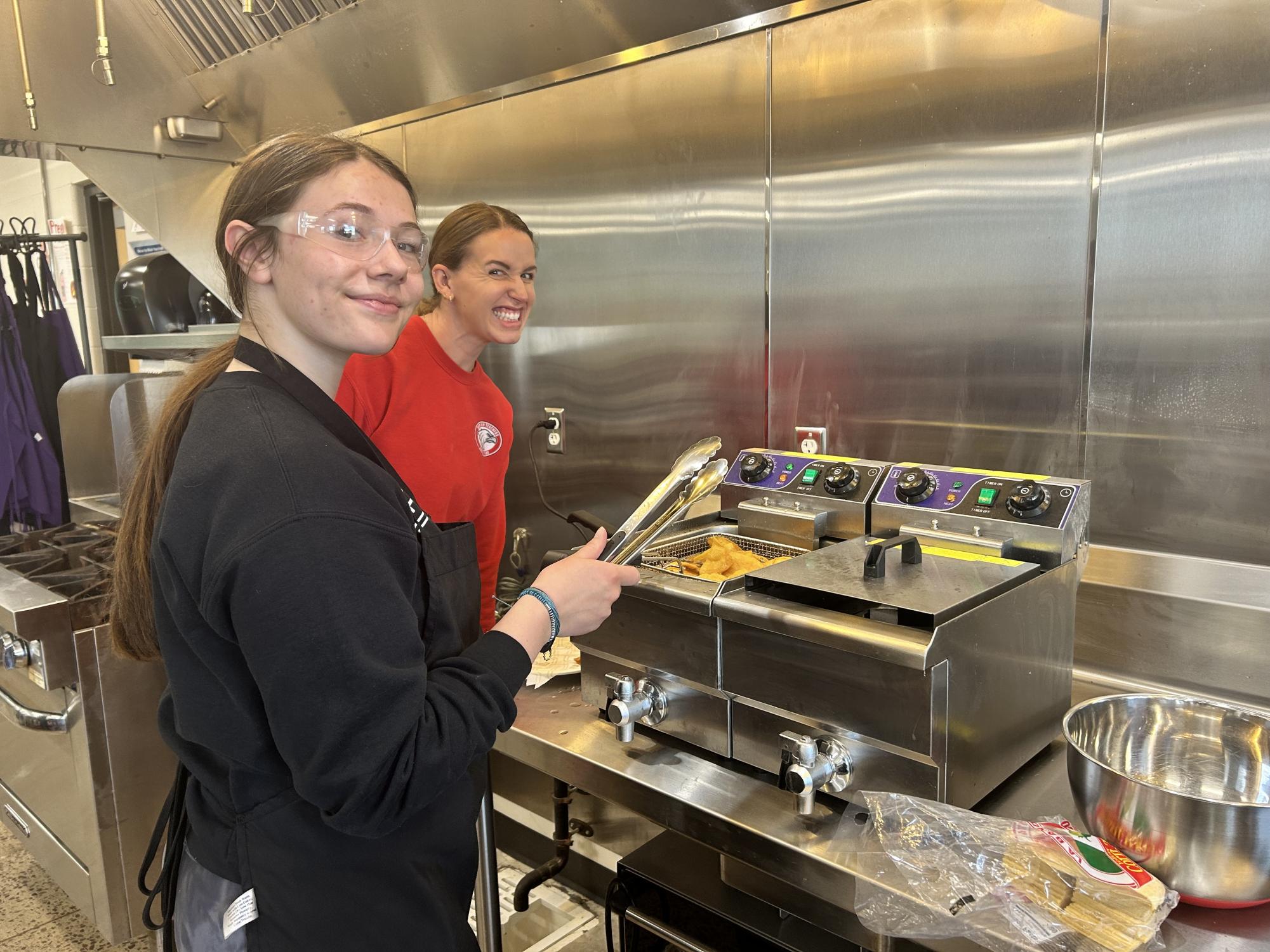 Brogan Hulke deep frying tortillas to make her fresh chips with Ms. Schneider assisting.